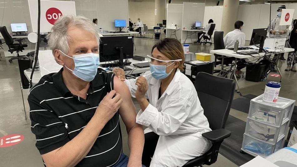 雷诺·加涅格(Renaud gagn<e:1>)戴着口罩，从戴着口罩和面罩的卫生保健工作者那里接受疫苗接种. 